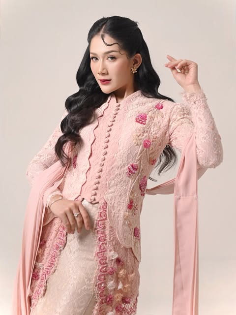 Model dengan rambut bergelombang panjang dan busana bordir pink.