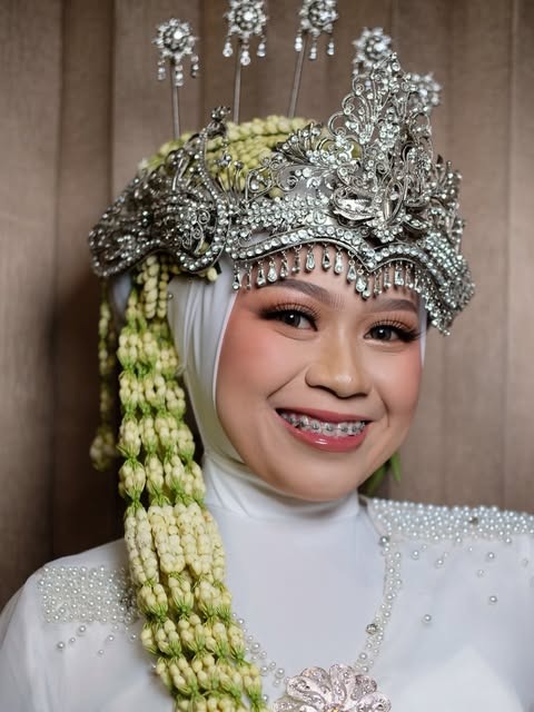 Pengantin dengan mahkota perak, rangkaian bunga, dan rias bibir pink.
