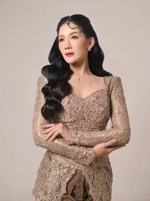 Model dengan rias mata tegas dan rambut bergelombang dalam busana emas kecokelatan.